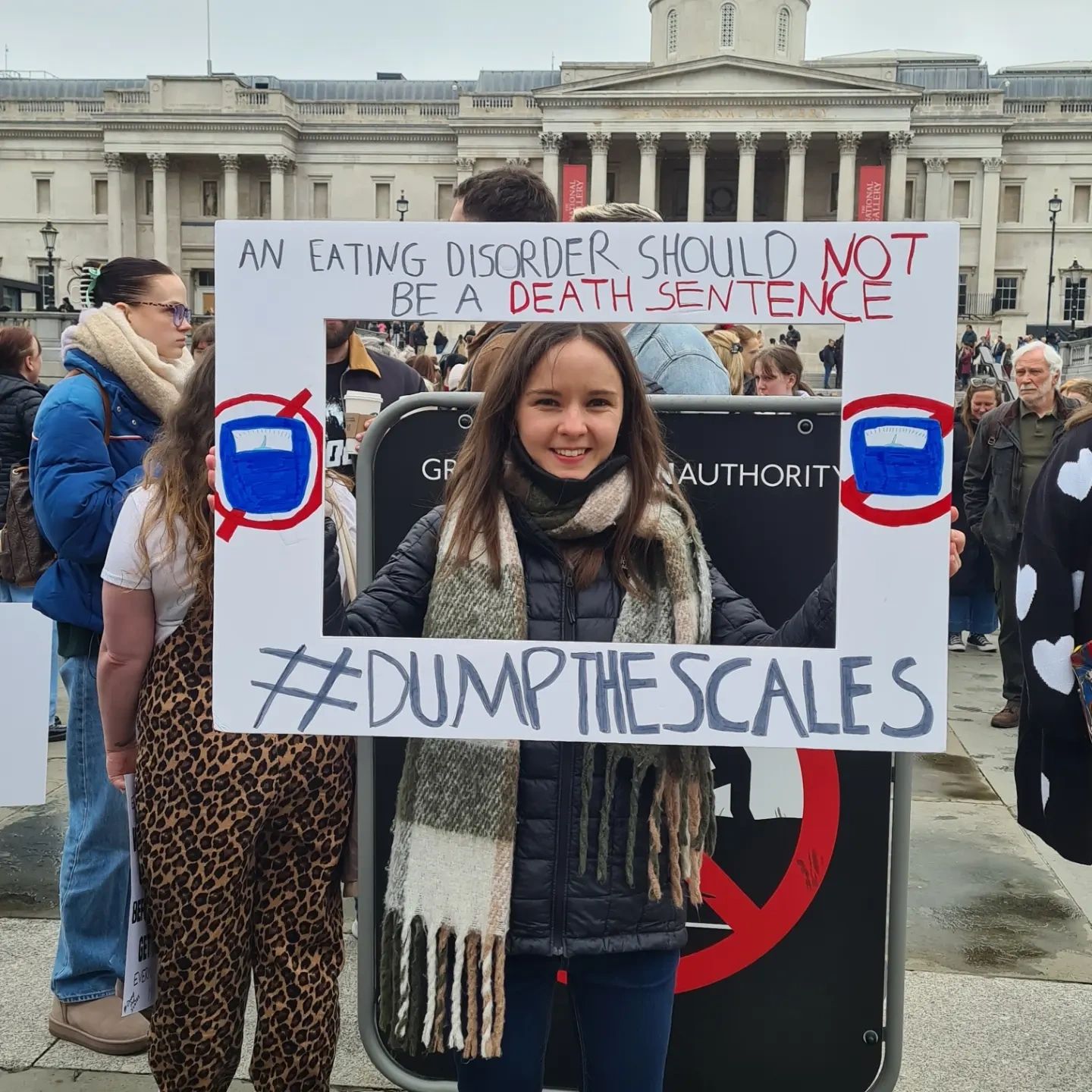 Rachel holds up a sign which says 'An eating disorder should not be a death sentence #Dumpthescales' at a protest march in Trafalgar Square, London, UK